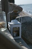 Burning candle in white lantern on tread of steps by the sea