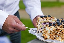 A man's hand hold a cake server with a piece of blueberry torte