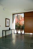 Modern foyer with large, grey tiles and floor-to-ceiling window next to front door