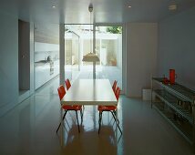 White dining table and orange shell chairs in minimalist room with view of courtyard