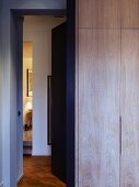 Wooden fitted wardrobe in bedroom next to open door with view of hallway