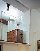 Antique chest of drawers behind half-height glass panels on gallery level