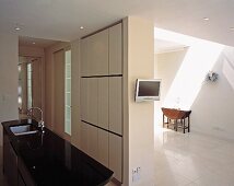Kitchen island with sink, television mounted on partition wall and console table under skylight