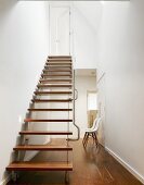 Designer staircase with wooden treads and stainless steel handrail in minimalist, open-plan stairwell