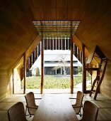 Wooden dining table with rattan chairs in wood-panelled room with view of Japanese courtyard