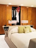 Bedside lamps on head of double bed in front of wooden fitted wardrobes with open door