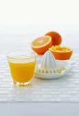 A glass of orange juice, citrus squeezer and oranges