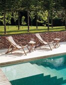 Deckchairs next to pool with masonry steps and lawn with trees