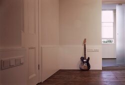 Guitar leaning on wall on floorboards in foyer
