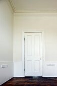 White-painted, panelled door and old floorboards in grand anteroom