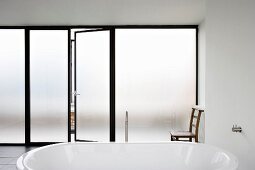 Free-standing bathtub in bathroom with floor-to-ceiling sliding doors in opaque glass