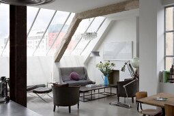 Open-plan living space with furniture in a mix of styles under glazed sloping ceiling