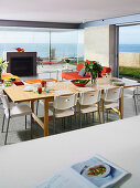 Living-dining room with glass walls with white plastic chairs around a set wooden table