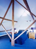 View through wooden structure of bed with blue bedspread and blue carpet in attic room