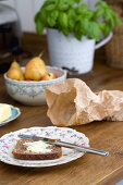 A slice of bread and butter on a nostalgic floral-patterned plate, next to a crumpled paper bag