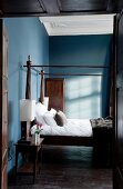 Antique canopied bed next to bedside table in blue-painted bedroom of old hunting lodge