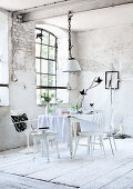 Dining table with tablecloth and white chairs in front of lattice window in dilapidated room in former factory