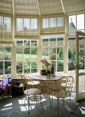 Delicate, white-painted metal table and chairs in vintage glass pavilion