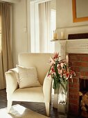 Elegant armchair with white cover and bouquet of lilies next to brick fireplace