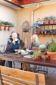 Coffee break in a courtyard - two laughing ladies at a garden table with a collection of cacti and iron wire wall shelves with plant pots