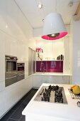 Kitchen with white cupboard doors and designer pendant lamp above gas hob in kitchen island