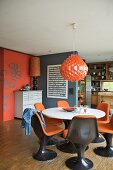 Brown plastic shell chairs with orange cushions and dining table below orange pendant lamp in open-plan room