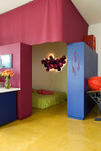 View into bedroom with futon and sculptural wall lamp separated from living area by cupboard partitions