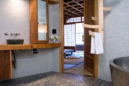 Simple bathroom with mosaic tiles on walls and wooden installations, open door with view of Japanese-style bedroom