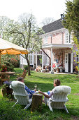 Ehepaar auf Holzsesseln mit Schaffell beim Weintrinken im Garten eines historischen, holländischen Landhauses