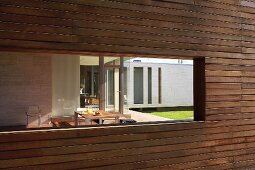 Window aperture in modern wooden facade with view of terrace table in front of contemporary house