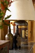 Zwei alte Flaschen als Dekoration neben Tischlampe mit antikem Metallbehälter als Leuchtenfuss