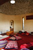 Bunte, indische Kissen auf rotem Teppich in Meditationsraum mit Kuppeldach aus Beton