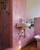 White sink on wall with claret mosaic tiles and open shower area in designer bathroom