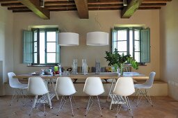 Dining area with white shell chairs and designer pendant lamps in renovated country house