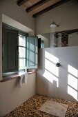 Designter Duschbereich im Landhaus - Wasser fließt aus Kopfbrause auf Bodensteinplatte und Kieselsteinfliesen