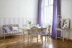 Alte französische Stühle um Holztisch im gustavianischem Stil und Sitzbank an Wand mit weissen und lila Streifen