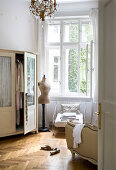 Kleiderschrank, Schneiderpuppe und alter Eisensessel vor offenem Fenster im Schlafzimmer einer Altbauwohnung
