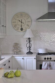 Nostalgic wall-mounted clock, wrought iron lamp base and pyramid of pigs decorating white, country house kitchen