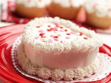 Kleiner herzförmiger Kuchen mit weißem Zuckerguss und Zuckerherzen