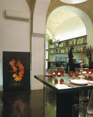 Festively set table with elegant red wine glasses; woman using laptop in background of modern studio within historic walls