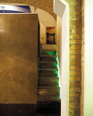 Narrow stairs with indirect lighting leading to gallery on cubic room-in-room installation below historic brick vault