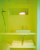 Bathroom niche bathed in yellow light with square counter-top basin on open washstand with towel shelf