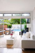 Corner of designer living room with white leather sofa and low minimalist coffee table in front of open terrace door with view of pool