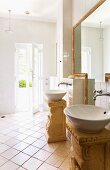 Two round sinks on free standing, Roman style pedestals in a light and bright bathroom with an entrance to a garden area