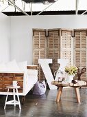 Rustic, wooden coffee table in front of sofa on castors and screen against partition wall