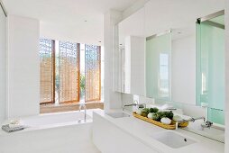 Puristisches Badezimmer mit Doppelwaschtisch und Badewanne vor drehbaren Rattanelementen als Sichtschutz