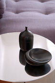 Schwarz glasierte Keramikgefässe auf der spiegelnden Metallplatte eines Beistelltisches; Sofa-Ausschnitt im Hintergrund