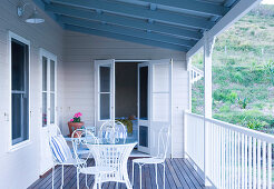 Table with decorative white metal chairs on the veranda of a wooden home