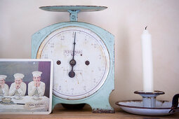 Post card in front of a vintage scale and candlestick holder and candle on a shelf