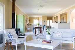 Simple living-dining room with armchair and sofa around a coffee table in front of a cast iron stove